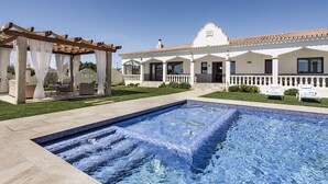 A pool with a pergola and outdoor seating area, a white building with a tiled roof, and a clear blue sky. - Flor de Lis - VIP Properties by Interhome (Paderne)