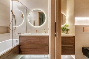 A modern bathroom with a glass-enclosed shower, wooden vanity, and two round mirrors.