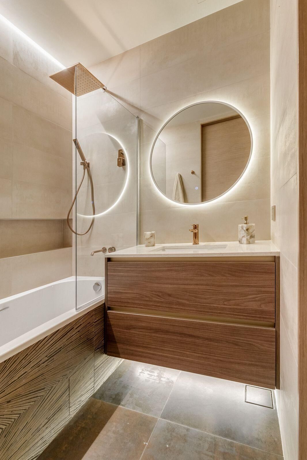 Ein modernes Badezimmer mit einer gläsernen Duschkabine, einem runden Spiegel mit integrierter Beleuchtung, einem Holzwaschtisch und einer Badewanne.