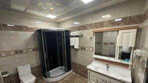 A bathroom with a toilet, a shower enclosure, a sink, and a mirror. - Raymond Hotel (Baku)