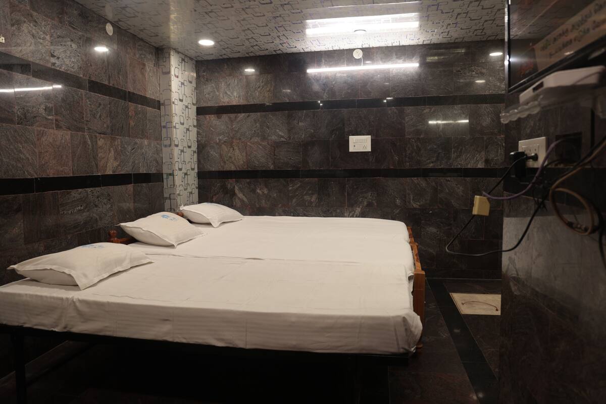 Hotellihuone, jossa on sänky, tyynyjä, yöpöytä ja seinälle asennettu puhelin.