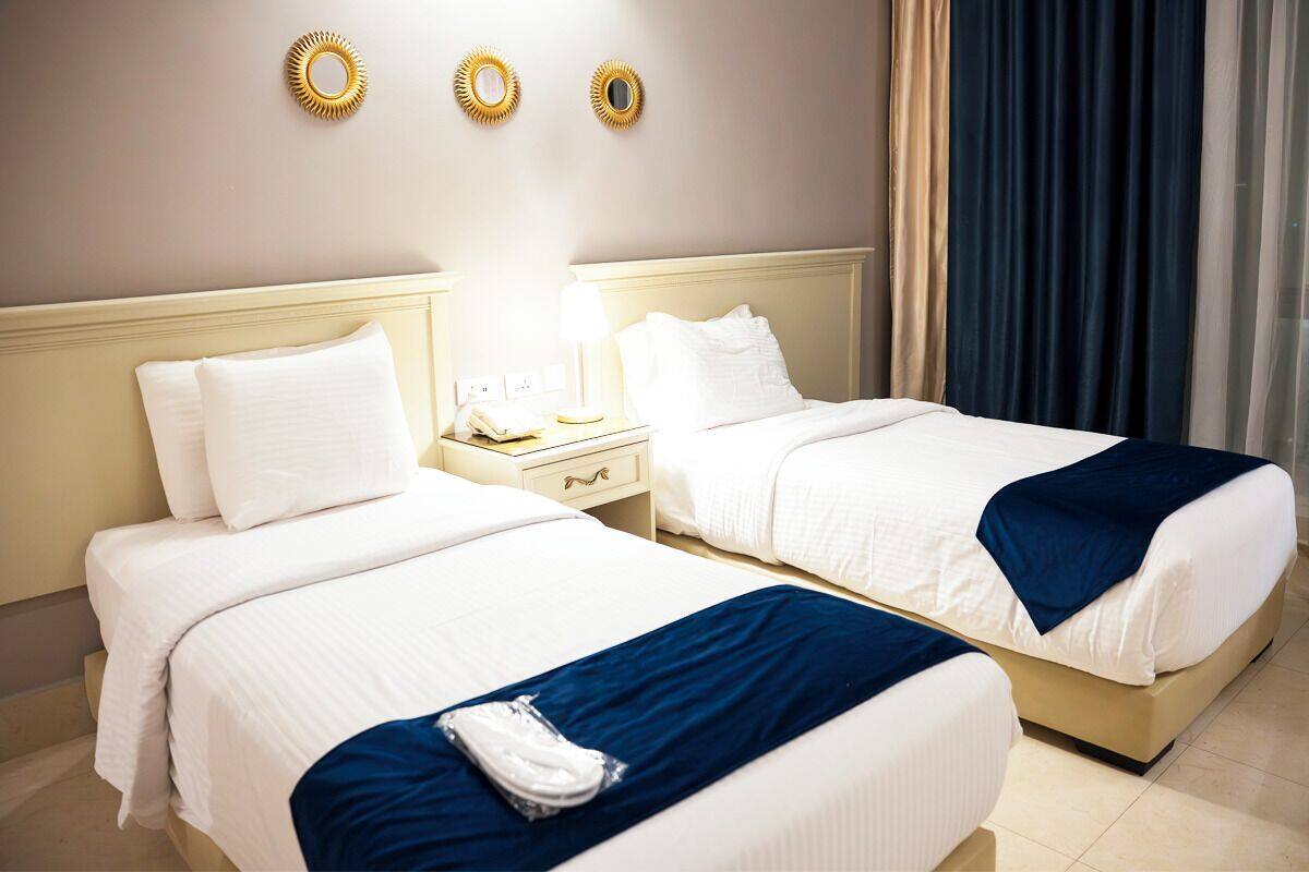Habitación de hotel con dos camas, una mesita de noche, una lámpara y una ventana con cortinas.