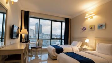 A hotel room with two beds, a desk, a chair, a TV, and a large window with a city view.