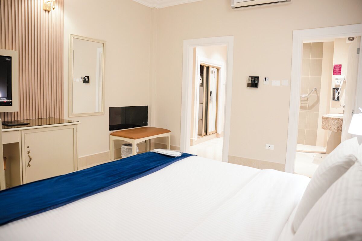 A hotel room with a bed, a desk with a computer, a TV, and a bathroom visible through an open door.