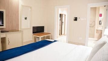 A hotel room with a bed, a desk with a computer, a TV, and a bathroom visible through an open door.