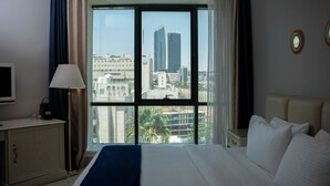 Una habitación de hotel con un ventanal grande, una cama, una mesita de noche, una lámpara y un televisor.