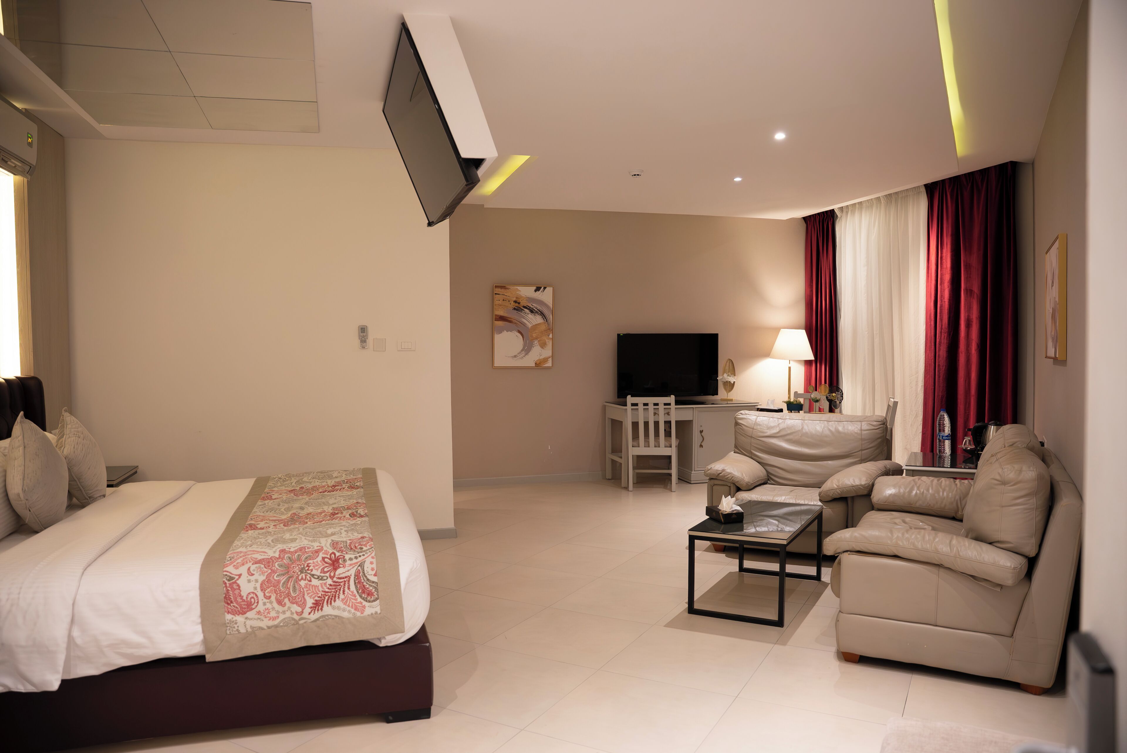 A hotel room with a bed, a sofa, a TV, and a desk with a lamp.