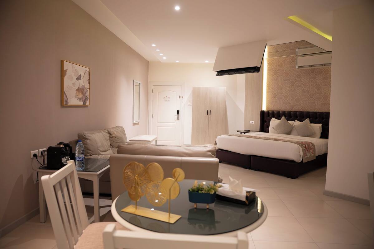 Una habitación de hotel moderna con cama, sofá, mesa de comedor y una pequeña cocina.