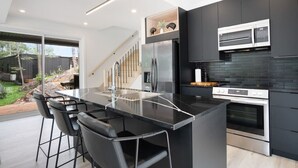 A modern kitchen with a central island, black bar stools, a stainless steel refrigerator, and a built-in oven.