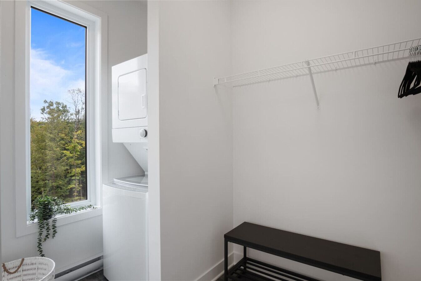 A laundry room with a window, a washing machine, a drying rack, and a bench.