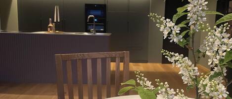 A modern kitchen with a central island, wooden chairs, and a vase with white flowers.