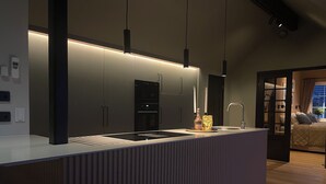 A modern kitchen with a central island, built-in appliances, pendant lighting, and a view into a bedroom. - Panoramic view near Gbg and nature (Västra Götalands län)