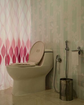 A bathroom with a toilet, a shower, and a trash can. - Mandawara - Shri Orchard House (Kullu)