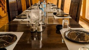Une longue table à manger, dressée pour un repas, se trouve dans une pièce aux poutres apparentes et dont les murs sont ornés d’œuvres d’art encadrées.