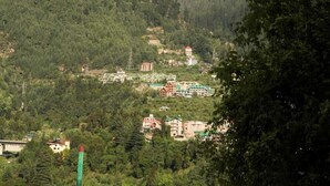 Un paysage montagneux avec un arc-en-ciel, une forêt dense et un petit village avec quelques bâtiments.