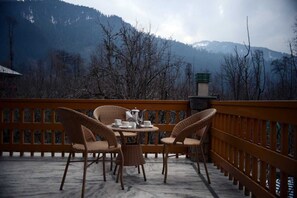 A terrace with wicker chairs and a table set for tea, overlooking a mountainous landscape. - Mandawara - Shri Orchard House (Kullu)