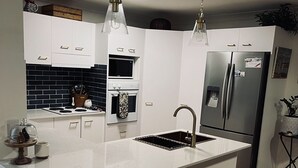 Una cocina moderna con armarios blancos, una isla central con un fregadero, un refrigerador de acero inoxidable y un microondas.
