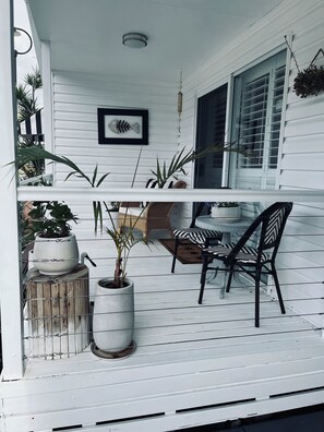 Une véranda blanche avec une table et des chaises, des plantes en pot et un tableau représentant un poisson.