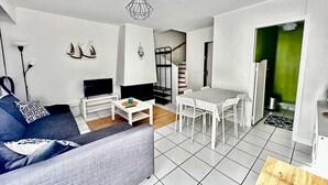 A modern living room with a sofa, TV, and a dining table with chairs. - La "Casita", triplex with garden near the center of town (Courseulles-sur-Mer)