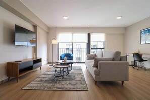 A modern living room with a sofa, coffee table, TV, and a large window.