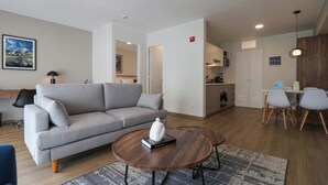 Een moderne woonkamer met een grijze bank, een ronde salontafel met een boek, en een eethoek met een tafel en stoelen.