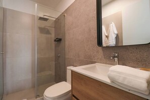 A modern bathroom with a glass shower enclosure, a white toilet, and a wooden vanity with a white sink and a towel.