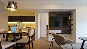 A modern dining area with a round table, four chairs, and a hanging light fixture. A kitchen is visible in the background, and a flat-screen TV is mounted on the wall. - w* | Comfy 2BR w/ Balcony Near Larcomar (Miraflores)