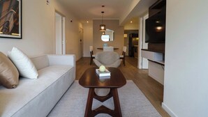 A modern living room with a sofa, a coffee table, and a chair. There is a television mounted on the wall, a dining table with chairs, and a kitchen area in the background. - w* | Comfy 2BR w/ Balcony Near Larcomar (Miraflores)