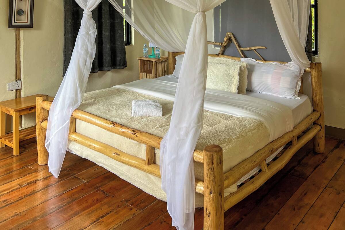A wooden bed with a white canopy, a wooden nightstand, a framed picture on the wall, and a window with curtains.