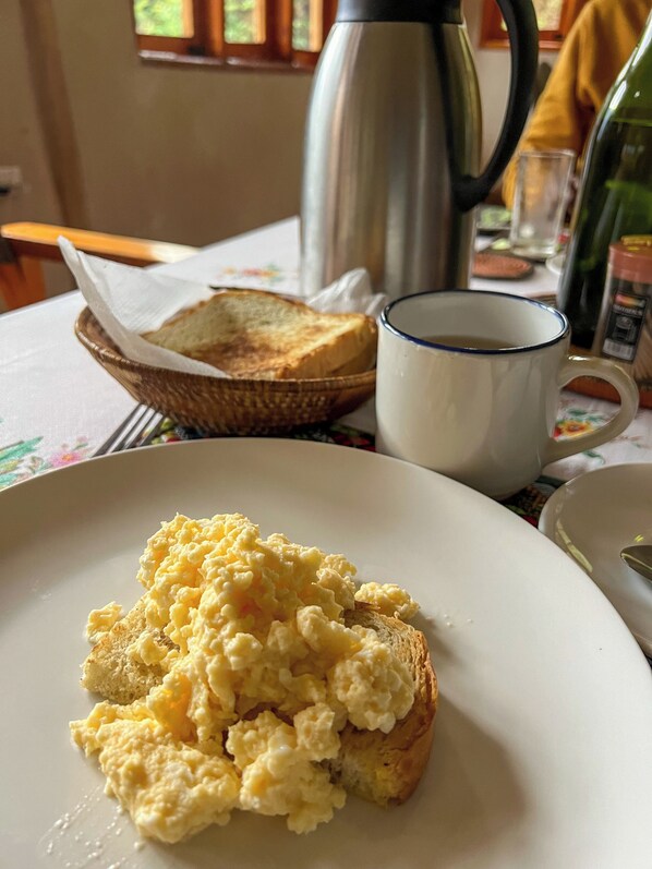 Huevos revueltos sobre tostadas, una taza de café y una cesta con pan en una mesa.