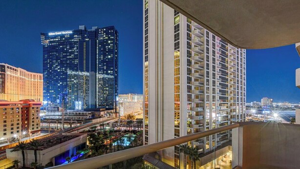 A high-rise hotel with multiple floors and balconies, a pool area, and a view of the city skyline at night. - Premium Studio | Jacuzzi, Balcony & Strip View (Las Vegas)