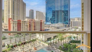 A hotel with a modern glass facade, a pool area with lounge chairs, and a view of surrounding high-rise buildings. - Premium Studio | Jacuzzi, Balcony & Strip View (Las Vegas)
