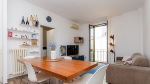 A modern living room with a wooden dining table, white chairs, a brown sofa, and a TV. - VivimiHome - Stelvio House (Milano)