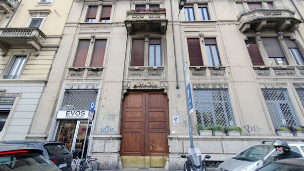 A historic building with a large wooden door, a sign for 'EVOS PARRUCCIERI', and a parking sign. - VivimiHome - Stelvio House (Milano)