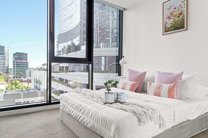 A bedroom with a large window, a bed with white bedding, and a city view. - Chic City Views Modern Comfort Near Southern Cross (Melbourne)