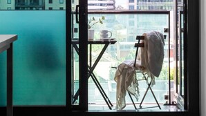 A balcony with a view of city buildings, a folding chair, and a table.