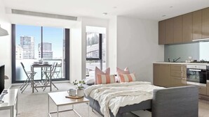 A modern bedroom with a bed, bedside table, and a view of the city through large windows.