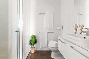 A modern bathroom with a glass shower enclosure, white tiles, a toilet, a sink with a mirror, and a potted plant. - Chic City Views Modern Comfort Near Southern Cross (Melbourne)