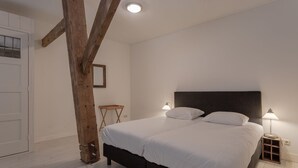 A bedroom with a large bed, two bedside lamps, a wooden chair, and a white door. - Cozy apartment in a former farm within walking distance of the center of Workum (Workum)