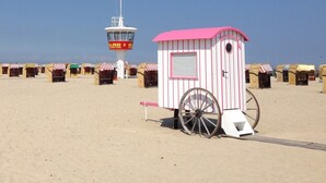 A beach with a lifeguard tower and a small pink and white structure with a wheelbarrow. - Modern apartment with exceptional sea view and balcony in Travemünde (Lübeck)