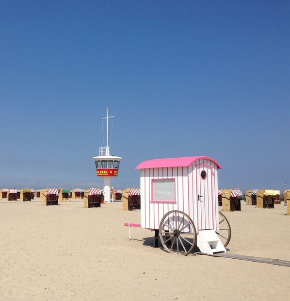 Una playa con una torre de salvavidas y una pequeña estructura rosa y blanca con una carretilla.