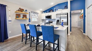 Una cucina moderna con mobili bianchi, un frigorifero in acciaio inossidabile e un'area pranzo con sedie blu.