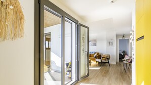Un intérieur moderne avec une porte-fenêtre coulissante donnant sur un espace de vie, un mur d’accent jaune et un plancher en bois.