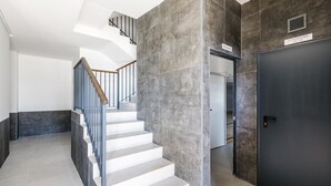 Un escalier moderne avec une rampe en bois, une porte sombre portant l’inscription « CONTADORES DE LUZ » et une enseigne au-dessus de la porte.