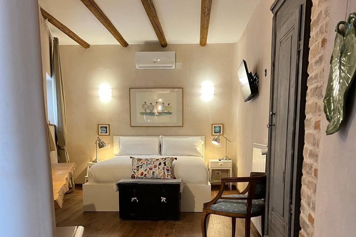 A cozy hotel room with a bed, a desk, a chair, a suitcase, and a wardrobe.