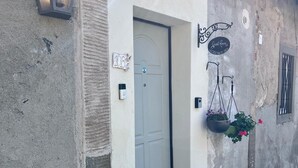 A building with a white door, a small porch, a hanging plant, and a wall-mounted sign. - La Cascina di Bea (Torre Boldone)