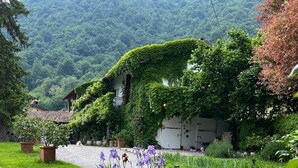 A garden with a pathway leading to a traditional building, surrounded by lush greenery and purple flowers. - La Cascina di Bea (Torre Boldone)