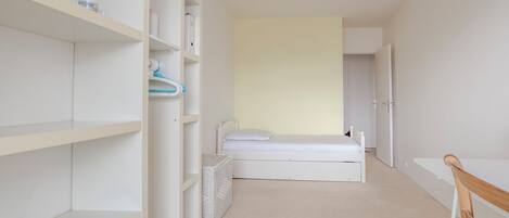Une chambre avec un lit simple, une armoire blanche et un petit bureau.
