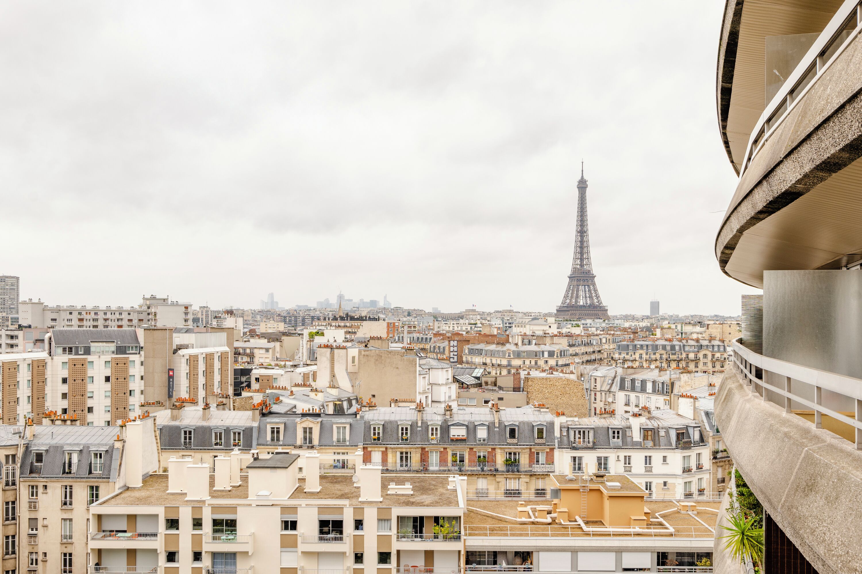 Un immeuble de grande hauteur doté de nombreux balcons, qui offre une vue sur une zone urbaine densément peuplée, avec la Tour Eiffel visible au loin.