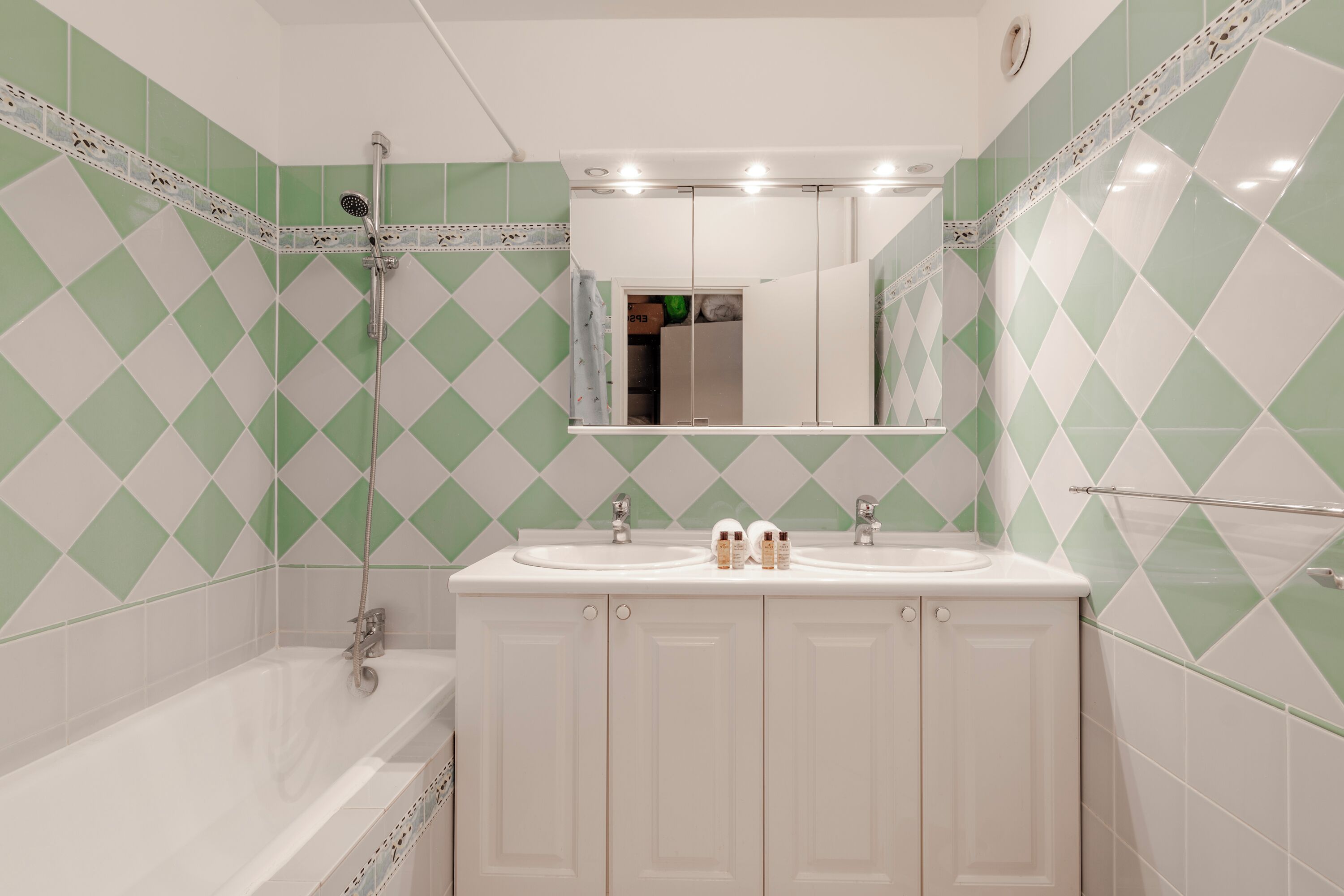 Een badkamer met een wit bad, twee wastafels en een spiegel boven de wastafels.